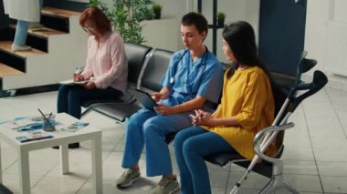 Koltuk değnekli Asyalı kadına danışmanlık yapan tıbbi asyalı kadın sağlık raporu doldurmak ve sağlık sigortası almak için dijital tablet kullanıyor. Fiziksel engelli hasta hemşireyle konuşuyor..
