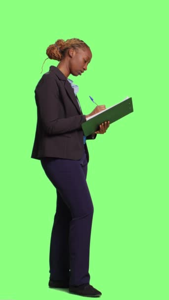 垂直视频 办公室员工在绿色屏幕背景下的文件上做笔记 在剪贴板上写信息和公司数据 作为经理工作的妇女的全身绿色屏幕 — 图库视频影像