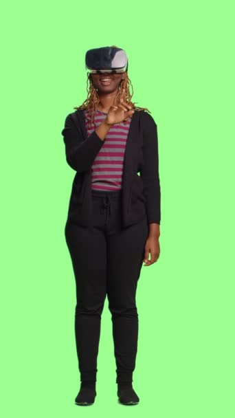 垂直视频 使用Vr眼镜的女性模特站在全身上下的绿色屏幕背景上 玩乐于虚拟现实耳机 在绿屏上享受科技和人工智能 — 图库视频影像