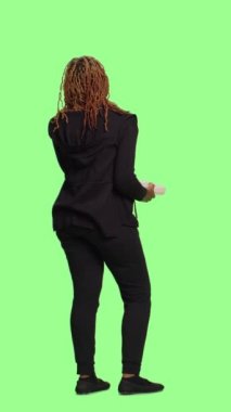 Dikey video: Genç yetişkin, yeşil ekran arkaplanı üzerinde tüm vücuduyla sabit telefon görüşmesi yapıyor, yeşil ekran arkaplanda duruyor. Kabloyla ofis telefonunda sohbet etmek, neşeli ve iyimser olmak.