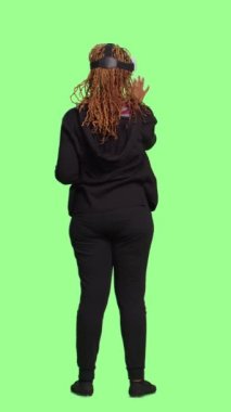 Dikey video: Modern insan vr kulaklık kullanarak tüm vr yeşil ekran arkaplanının üzerinde duruyor, sanal gerçeklik 3d gözlüklerinin keyfini çıkarıyor. Yeşil ekran arka planında yapay zeka ile oynanıyor.