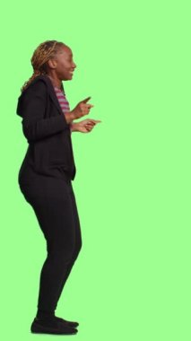 Dikey video: Genç pozitif yetişkin dansı ve stüdyoda yeşil ekranın arkasında aylak aylak dolaşmak. Aptal neşeli kadın dans ederken tüm vücudunu yeşil ekrana yansıtıyor.