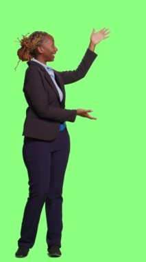 Dikey video: Afrikalı Amerikalı iş kadını tüm yeşil ekran arkaplanı üzerinde yeşil ekran reklamı yapıyor. Stüdyo arka planında reklam ve promosyon sunan bayan yönetici, gülümseyen yetişkin