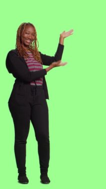 Dikey video: Yeşil ekran arkaplanı üzerinde kadın model reklam simgesi, yeşil ekran arkaplanı üzerinde tüm vücut. Gülümseyen kadın reklam yapıyor ve örnek olarak izole edilmiş telif alanı reklamları yapıyor..