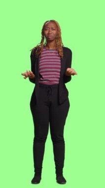 Dikey video: Kadın modelin tüm vücudu izole edilmiş yeşil ekran arkaplanda belirsizlik işareti yaptığını bilmiyorum. Belirsiz karışık bir sembolle şüpheyi göstermek, yeşil perde arkaplanının üzerinde durmak.