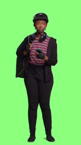垂直视频 女性承运人提供食物的背包和浏览互联网上的电话 站在全身绿屏背景 使用网上的电话网站提供快餐餐服务 — 图库视频影像