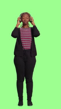 Dikey video: Modern insan kulaklıkla müzikten hoşlanıyor, tüm vücudu yeşil ekranda duruyor. Telsiz kulaklıklardan mp3 radyo şarkıları ve sesleri dinlemek, neşeli davranmak..