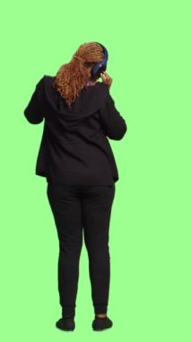 Dikey video: Mutlu kadın model kulaklıkla müzik dinliyor, tüm vücudu yeşil ekranda duruyor. Kablosuz kulaklıklarda radyo şarkıları ve seslerinin tadını çıkarmak, eğlenmek..