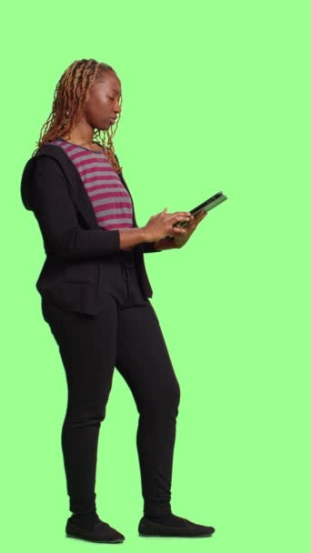垂直视频 快乐自信的女孩在绿屏背景上使用数字平板电脑 全身绿屏背景 在带有触摸屏 社交媒体应用的无线便携设备上浏览互联网 — 图库视频影像