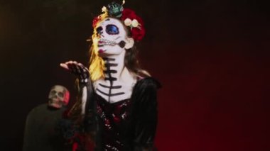 Ürkütücü güzellikteki manken kameraya hava öpücüğü yolluyor. Çiçekler takıyor, taç takıyor ve kafatası takıyor. Öpücük yüzüyle makyaj yapıyor. La Cavalera Catrina 'ya benziyor, ölü gününde flört ediyor. El kamerasıyla..