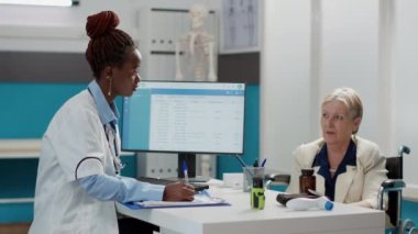 Kadın doktor, kadın hastalara reçeteli kâğıt veriyor, sağlık kontrolünde ilaç ve tedaviye yardım ediyor. Tekerlekli sandalyedeki engelli yaşlı hastaya tıbbi danışmanlık.