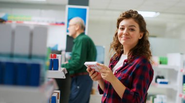 Eczanedeki ilaç ve vitaminlerle rafları inceleyen kadın müşteri, ilaç almak için ilave paketlere bakıyor. İlaç ürünlerini ve hapları kontrol ediyorum. El kamerasıyla..