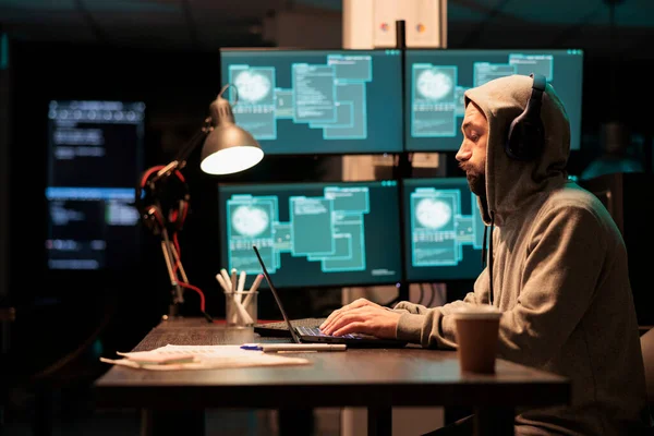 男性罪犯试图破坏数据库服务器 利用病毒对恶意软件进行编码 并在夜间窃取大数据 与多个监视器和黑客攻击信息系统一起工作 戴着头罩 — 图库照片
