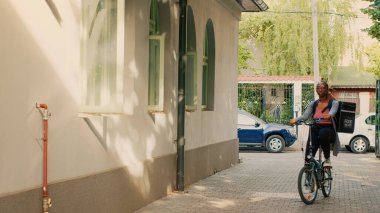 Bisikletli Afrika kökenli Amerikan kuryesi insanlara paket servis yapan bir kurye olarak çalışıyor. Bisiklete binen ve paket paket restoran yemekleri getiren bir kadın..