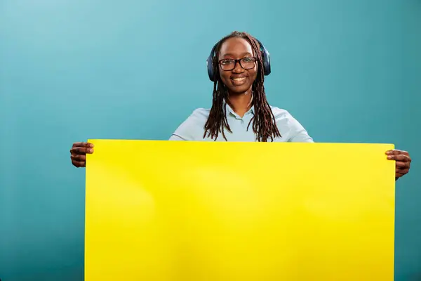Mavi Arka Planda Kablosuz Modern Kulaklıklar Varken Elinde Sarı Afiş — Stok fotoğraf