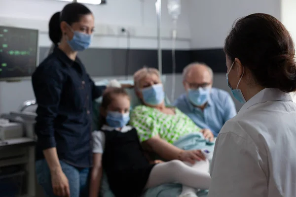 カバーアップを身に着けている認識できない医者は 患者の健康状態の進行を監視するための訪問室 コロナウイルス感染を防ぐために祖母病院の寝室に医療用マスクを着用する家族 — ストック写真