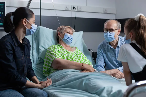 家族との手術を待っている高齢女性 親戚は観察中の老婦人と病院の部屋でチャットしています 診療所の訪問者を受け取るベッドのシニア女性 — ストック写真