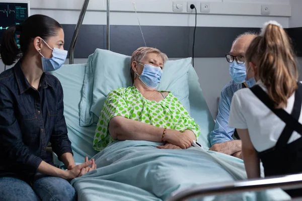 老人夫婦は病院の部屋で若い女性と娘とおしゃべりをする 診療所での手術から回復するシニア女性 親戚の会社を楽しんで寝たきりの老女 — ストック写真