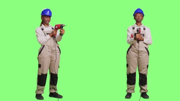 全身の緑の画面の背景にパワードリルや爪銃を保持制服やハード帽子の女性の請負業者 全体とヘルメットを身に着けて 改装し 再装飾するために掘削銃を使用して — ストック動画