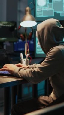 Dikey video: Geceyarısı bilgisayar sunucusunu maskeyle hackleyen sahtekar, bilgi çalmak için dizüstü bilgisayar ve çoklu monitör üzerinde çalışıyor. Siber kimlikli gizemli maskeli bir hırsız.