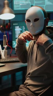 Dikey video: Maskeli dolandırıcı gece geç saatlerde bilgisayar ağını hackliyor, bilgi çalmak için laptop ve çoklu monitörler üzerinde çalışıyor. Gizli kimlik kıran hackerlar güvenlik sunucusu, siber
