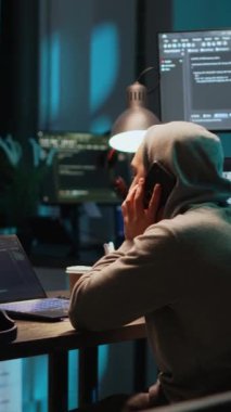 Dikey video: Genç programcı ofisteki telefona cevap veriyor, akıllı telefonla konuşuyor ve kullanıcı arayüzü kodluyor. Cep telefonu hattında uzaktan konuşma yapmak, terminal penceresinde html betiği kullanmak.