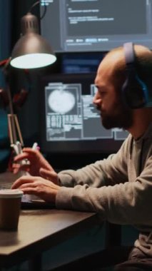 Dikey video: Müzik dinleyen, davul çalan, ofiste oynaşan komik programcı. Genç erkek kodlayıcı enstrümanla eğleniyor, aptalca davranıyor ve kulaklıkla şarkı söylüyor..