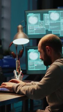 Dikey video: Programlama hırsızı gece geç saatlerde ofiste başarıyı kutluyor, birden fazla monitörle şifre çalmak için çalışıyor. Gizli kimliği olan neşeli bir bilgisayar korsanı.