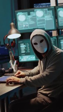 Dikey video: Erkek suçlu bilgisayar sistemini hacklemek için maske takıyor, büyük verileri çalmak için şirket sunucularına giriyor. Maskeli adam tehlikeli ve korkutucu görünüyor, sahtekar güvenlik yazılımı yaratıyor.