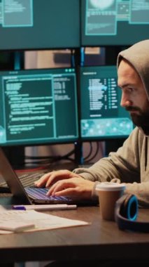 Dikey video: Hırsız siber güvenlik sistemini aşıyor ve birden fazla monitörden veri çalıyor. Kapüşonlu tehlikeli bir hacker kahve içiyor ve virüslü bir bilgisayar sunucusuna kötü yazılım yüklüyor..