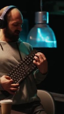 Dikey video: Programcı mutlu ve klavye enstrümanıyla gitar çalıyor, müzik veya şarkıdan hoşlanıyor ve eğleniyor. Genç, neşeli yetişkin davranışları. Gece geç saatlerde ofiste aptalca davranışlar..