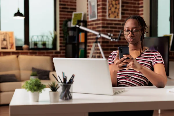 若いアフリカ系アメリカ人女性がスマートフォンにテキストメッセージを送信し ソーシャルメディアネットワークで通信する 仕事を休んでいるリモートワーカー 携帯電話でインターネットサーフィン — ストック写真