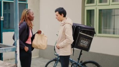 Afro-Amerikalı müşteri fast food siparişini kredi kartıyla ödüyor, bayan kurye postal terminalini tutuyor. Müşteri postacıdan yiyecek paketi almak için bağlantısız ödeme yapıyor..
