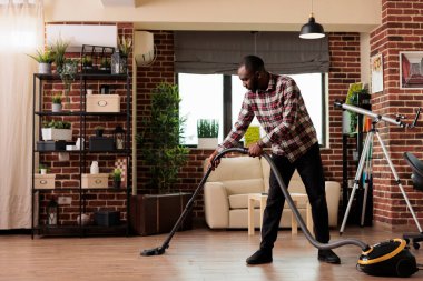 Kocası ev işleriyle ve temizlik işleriyle ilgileniyor, evdeki oturma odasının tozunu alıyor. Afro-Amerikalı adam ev işlerini özveriyle yapar, etrafı toplar ve düzenler..