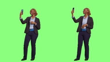 İş kadını fotoğraf çekiyor ve yeşil perde arkaplanının iki tarafındaki video görüşmelerine katılıyor. Online telekonferansta konuşmak ve fotoğraf çekmek için akıllı telefonu kullanmak, teknoloji..
