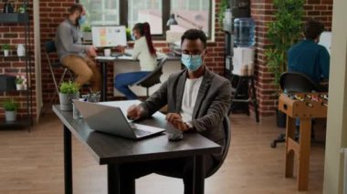 Ofis masasında dizüstü bilgisayarda çalışan Afrikalı Amerikalı iş adamı, başlangıç sunumunu planlamak için online araştırma verilerini kullanıyor. Çalışan covid 19 salgını sırasında profesyonel e-posta gönderiyor.