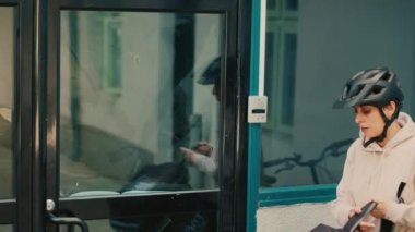 Kadın taşıyıcı ofisin ön kapısındaki kadına fast food siparişi veriyor, hızlı teslimat. Kadın müşteri, kuryeden kese kağıdında restoran yemeği alıyor. El kamerasıyla..