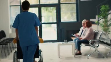 Tıbbi asistan tekerlekli sandalyedeki özürlü hastayı uzman doktorla kontrole götürüyor. Kronik bozukluğu olan Asyalı kadına yardım ve destek vermek. El kamerasıyla..