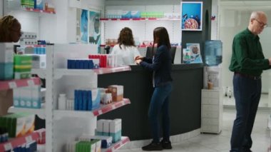 Sağlık uzmanı eczane tezgahındaki Asyalı müşteriye ilaç ve takviyelerden bahseden hap broşürlerini açıklıyor. Eczanedeki ilaç ürünleri konusunda müşterilere yardım eden işçiler.