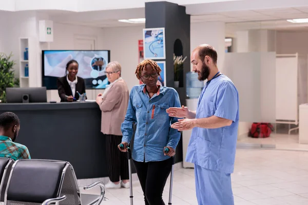 指导患变性疾病的非洲裔美国人前往治疗办公室的医院行政人员 支持老年妇女的疗养院的非洲女接待员 — 图库照片