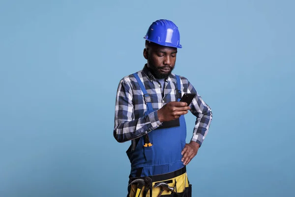 영국계 미국인 노동자 스튜디오에서 파란색 배경에 핸드폰을 사용하는걸봤어요 작업용 유니폼에 — 스톡 사진