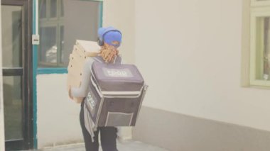 Fast food çalışanı, müşterilere yemek siparişi vermek için pizza kutusu yığını tutuyor. Yemek servisi. Telefondaki müşteri, pizzacı kuryeden yemek paketleri alıyor..