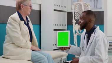 Elinde yeşil ekranlı dijital tablet olan erkek doktor, yaşlı kadına danışıyor. Sıhhiye ve hasta kromakey arkaplan ve boş telif boşluğuna sahip izole bir model şablonu inceliyor.