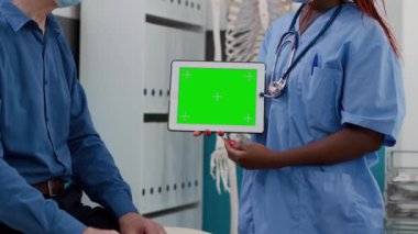 Specialist holding horizontal greenscreen on tablet at checkup with elderly patient. Using blank mockup display with isolated template and chromakey copyspace backgroung. Close up.