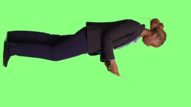 Dikey video: Diz üstü bilgisayarda çalışan kadın ofis çalışanı, yeşil ekran arka plan üzerinde çalışıyor, ofis kıyafeti giyiyor ve İnternet sitesine göz atıyor. Yönetici kablosuz bilgisayarı kullanarak kaydırır