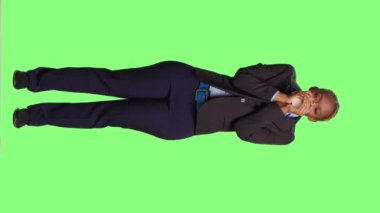 Dikey video: Stüdyoda kahve içen kadın ofis çalışanı, yeşil perde arkasında takım elbise giyiyor. Şirket müdürü içki ya da içecekten hoşlanıyor, şirket işine sahip..