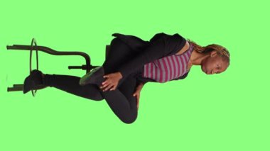 Dikey video: İyimser kadın model yeşil ekran arkaplanının üzerinde oturuyor, sırada bekliyor ve hazırlanıyor. Rahatlamış kadın, tüm vücudun yeşil ekran arka planına hazırlanıyor..