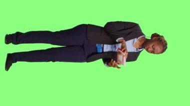 Dikey video: Hasta ofis çalışanı kardiyoloji ilaçları kutusuna bakıyor, tüm vücudun yeşil perde arkasında duruyor. İş kadını ilaç ve uyuşturucu etiketini kontrol ediyor.