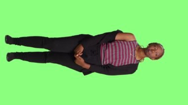 Dikey video: Sabırsız model yeşil ekran arkaplanı üzerinde yeşil ekran arkaplanı üzerinde bekliyor. Genç, neşeli kız bekle ve meraklı, modern, kendine güvenen yetişkin kadın rolü yap..