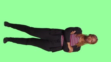 Dikey video: Afrikalı Amerikalı kadın yeşil ekran arka planında poz veriyor, tüm vücudu yeşil ekran şablonunda duruyor. İzole edilmiş krom anahtar arkaplan üzerinde doğal ve kendinden emin görünen kadın modeli.
